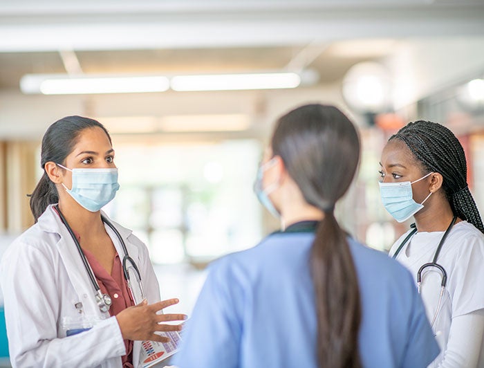 3 female medical personal talking together with masks on.