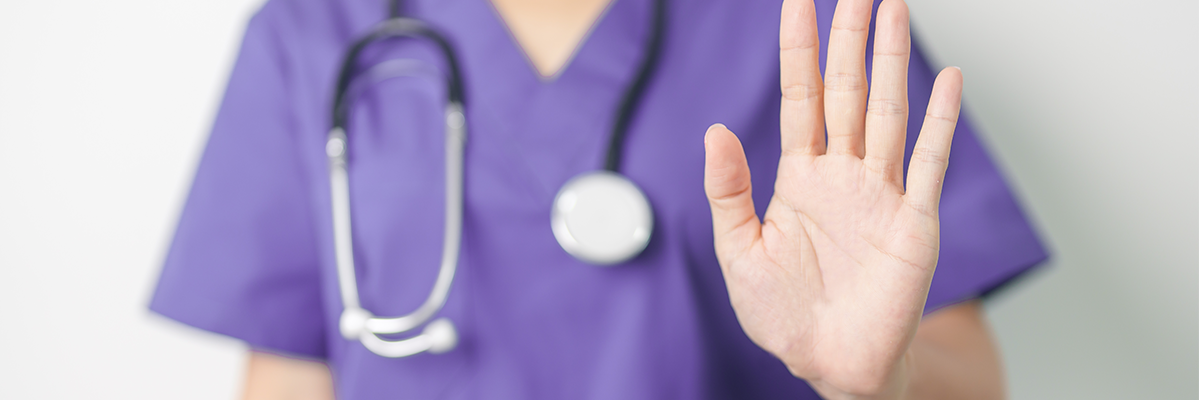 health care worker in scrubs wearing stethoscope with hand held up to signal stop 