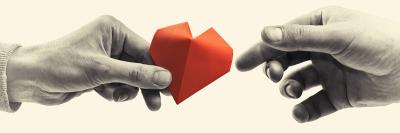 one hand passes a red paper heart to another hand